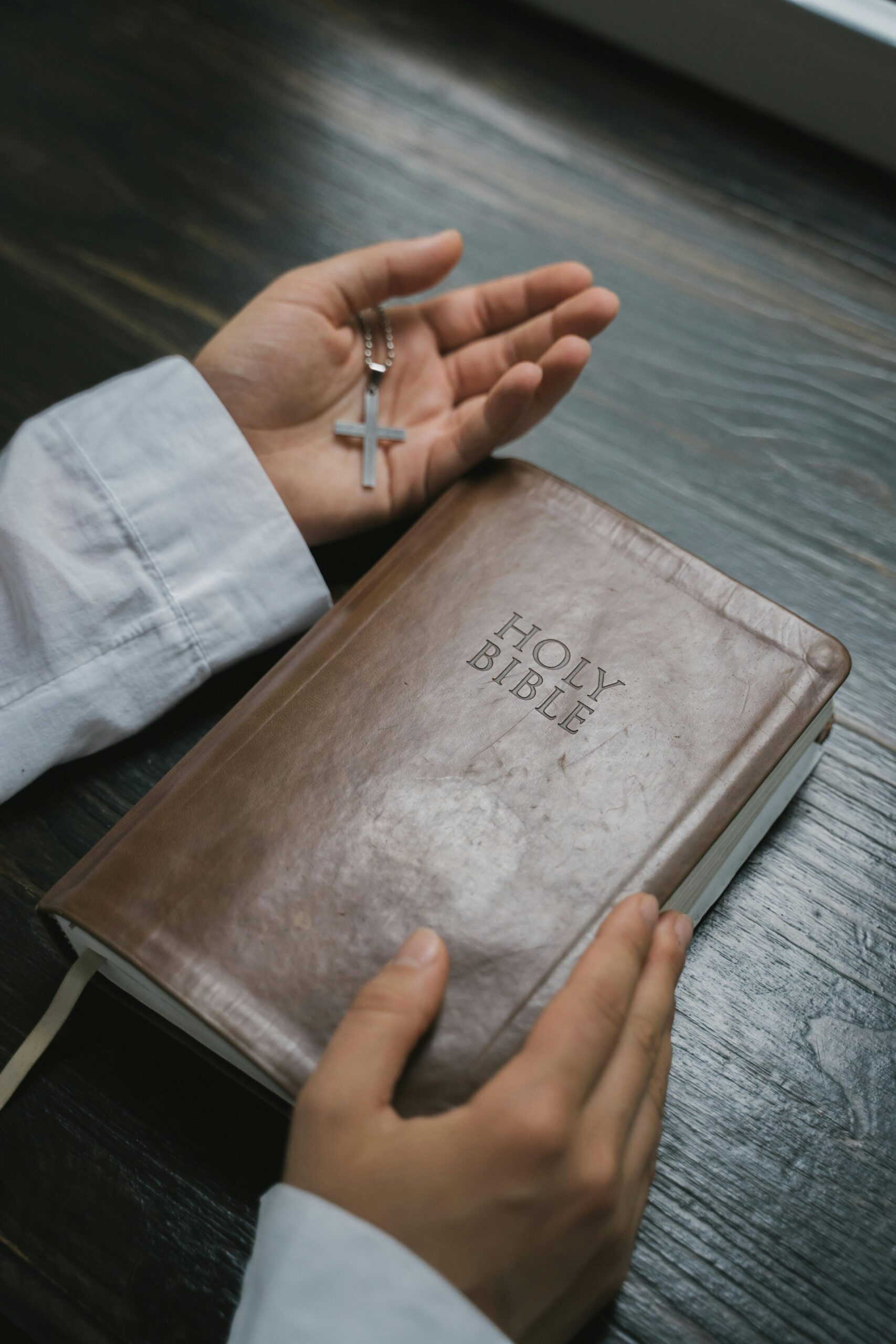 Close-up of hands holding a Holy Bible with a cross necklace, symbolizing faith and spirituality.